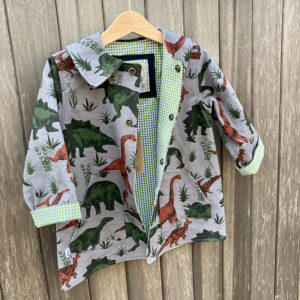 a grey child's jacket featuring large scale green and brown dinosaurs with a green cotton gingham lining
