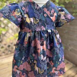 Toddler fantasy unicorn print dress with a wrap over front displayed outside on a mannequin.